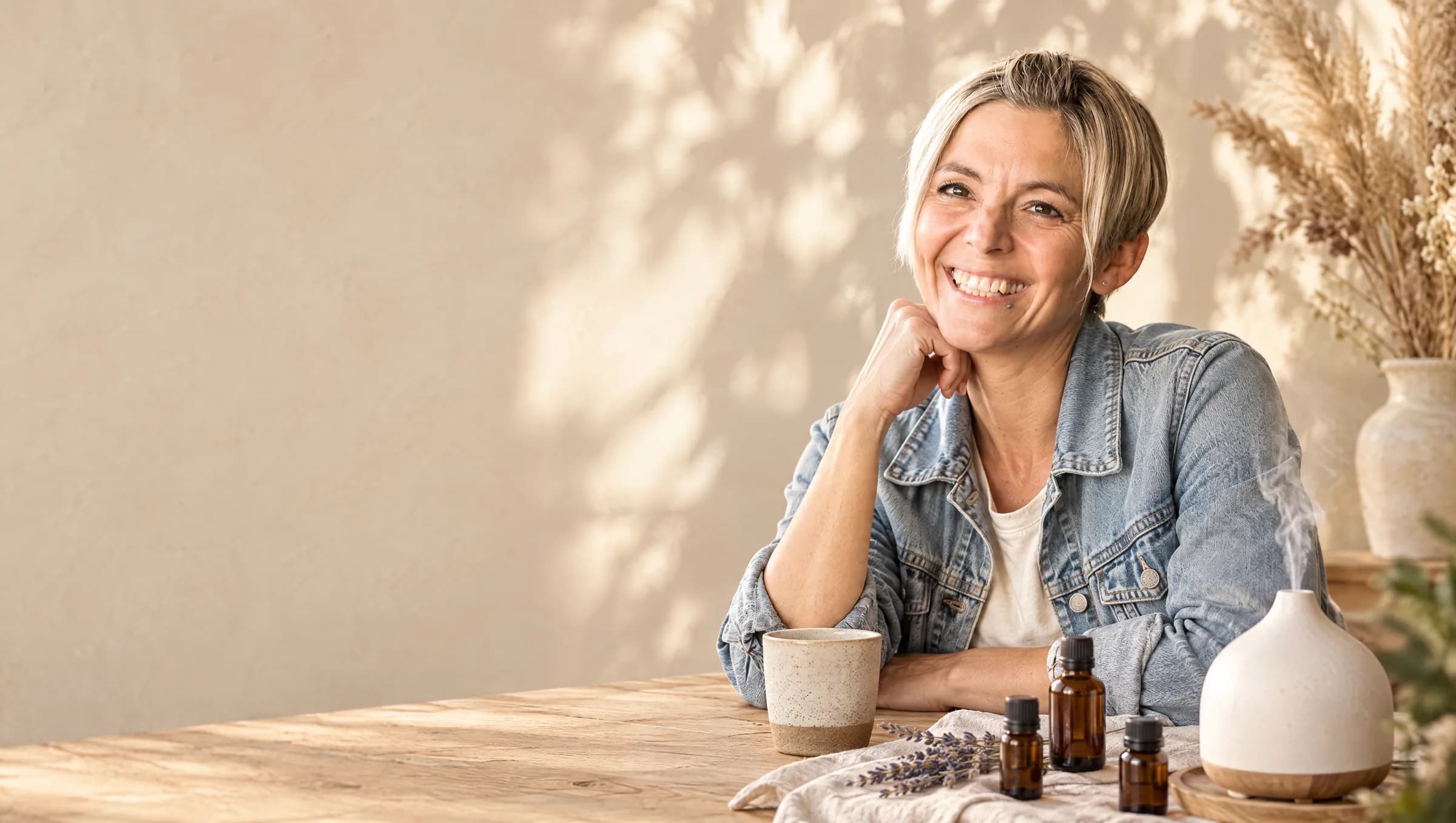 Caroline Amhof lachend am Holztisch mit Ölfläschchen und Diffuser